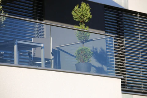 Façade moderne d'immeuble avec balcon vitré équipé de garde-corps en verre et structure métallique
