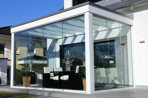 Véranda moderne entièrement vitrée avec structure aluminium blanc, intégrant salle à manger contemporaine avec table noire et chaises design