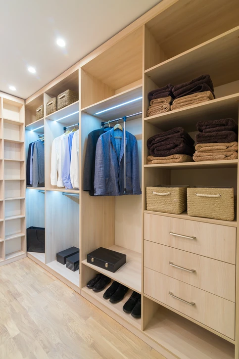 Dressing moderne avec aménagement sur mesure en bois clair, comprenant penderies avec éclairage LED intégré, étagères de rangement, tiroirs et compartiments pour chaussures